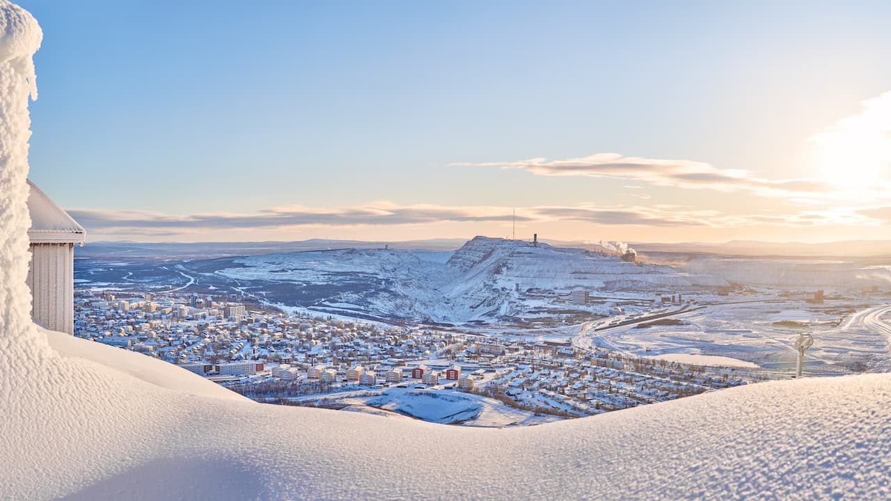 View of Kiruna city and the iron ore mine on the mountain Kiirunavaara seen from the snowy mountain peak Luossavaara.